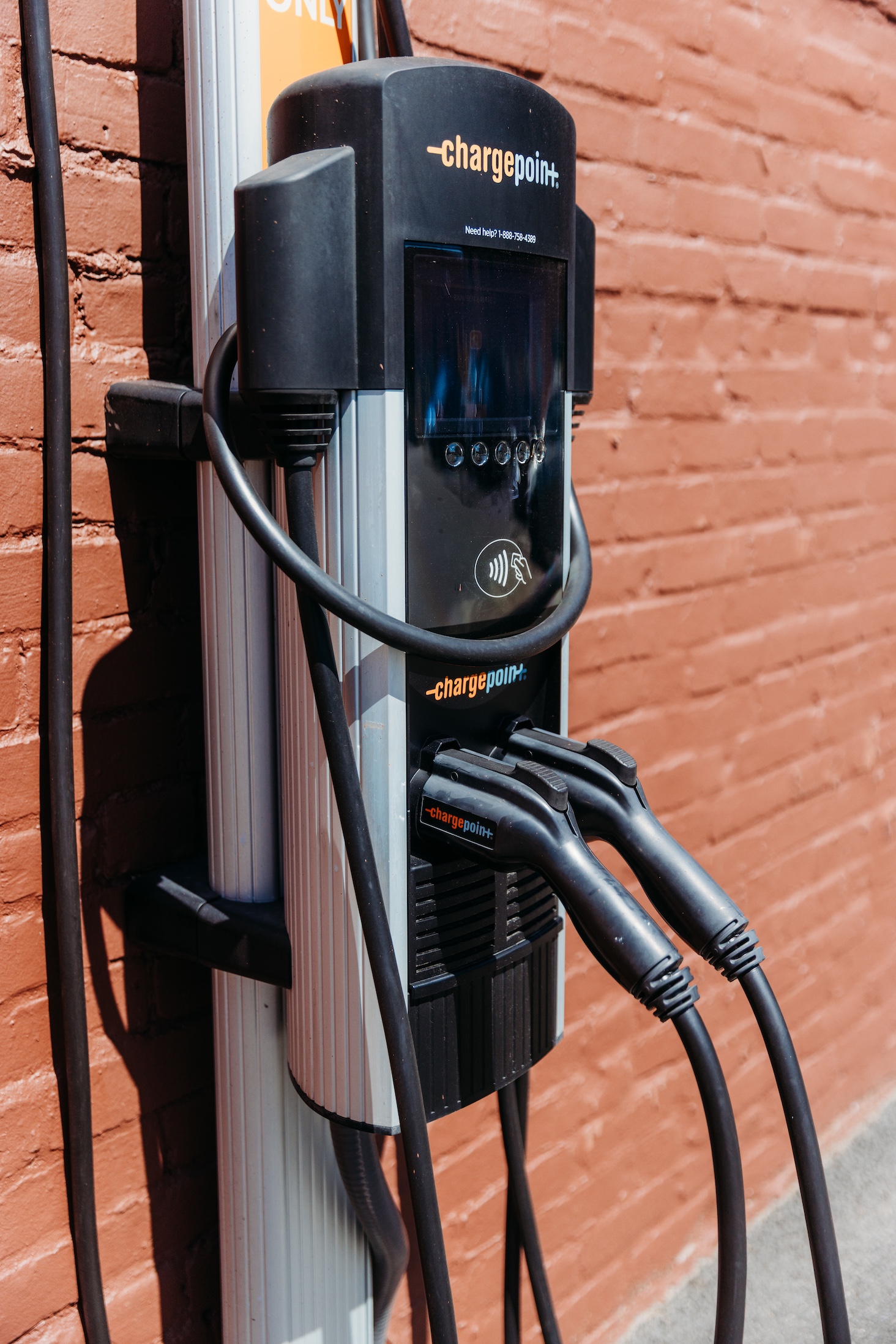 Electric vehicle charging station with two charging cables attached, mounted on a brick wall.