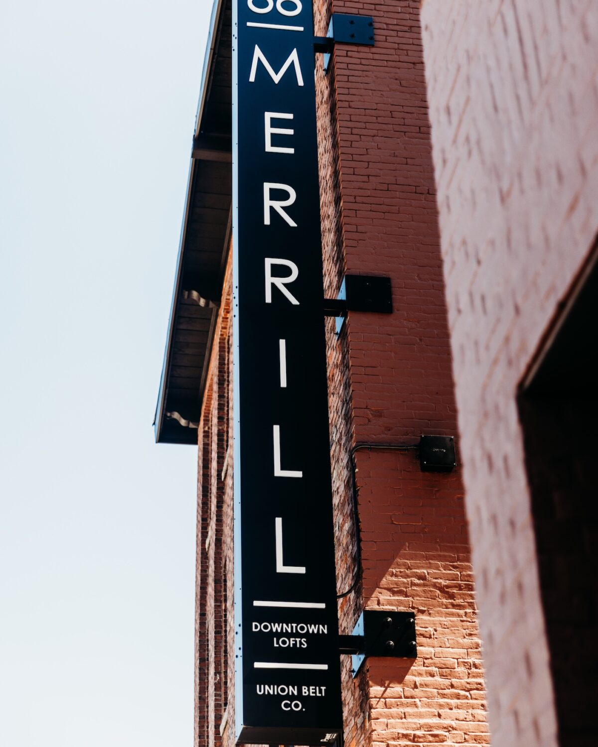 Sign for 66 Merrill, featuring "Downtown Lofts" and "Union Belt Co." against a brick wall.