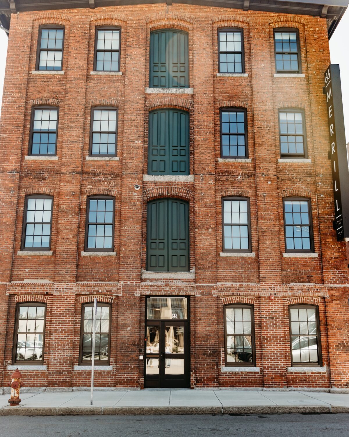 Brick building with green doors and large windows, featuring a sign that reads "MERRILL.