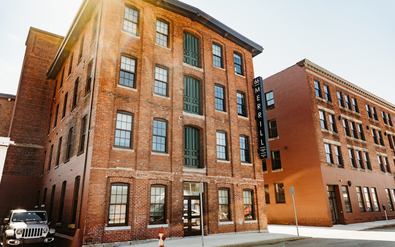 Brick building with large windows and a sign reading "66 MERRILL." A parked vehicle is visible nearby.