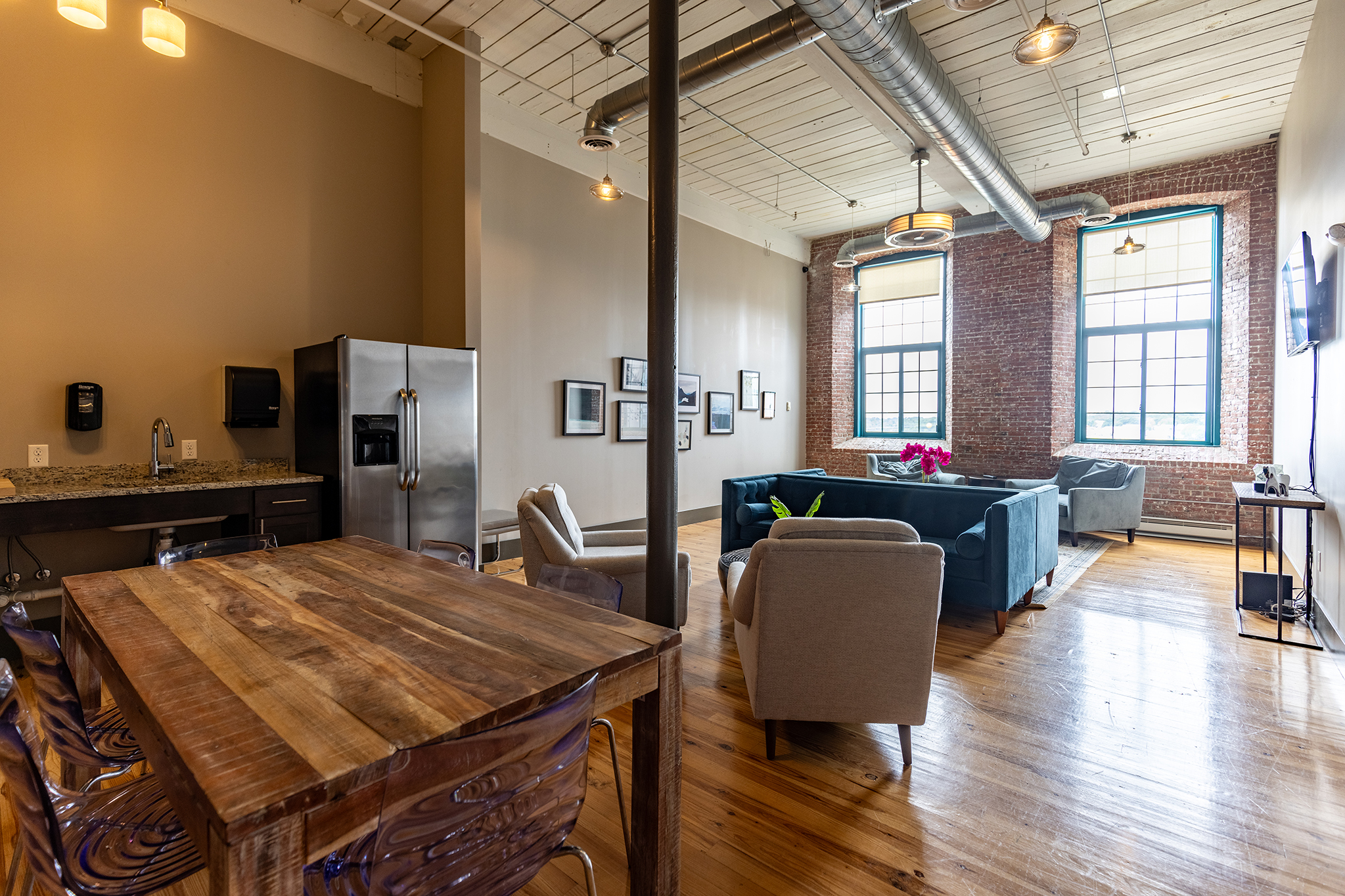Spacious living area with a wooden dining table, modern kitchen, and large windows. Cozy seating arrangements.