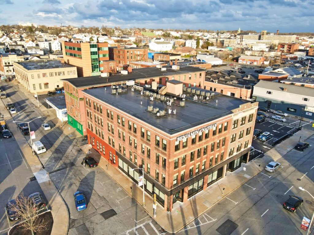 Aerial view of a brick building with "BENJAMIN" signage, surrounded by streets and parked cars.