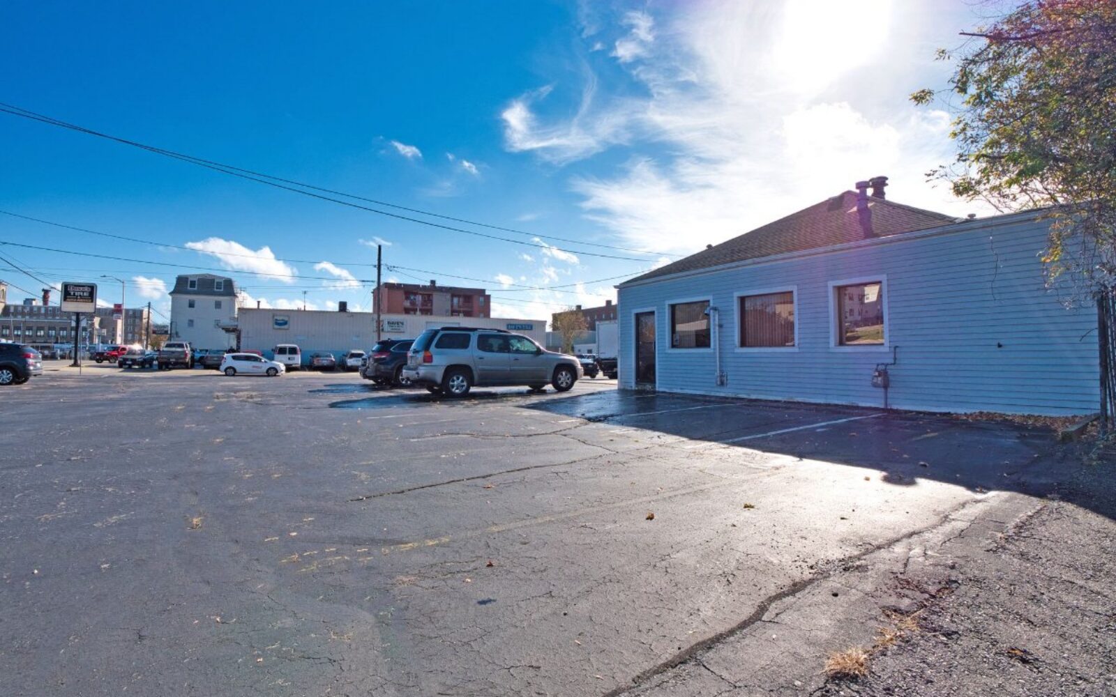 A blue building sits beside a parking lot filled with cars under a clear blue sky.