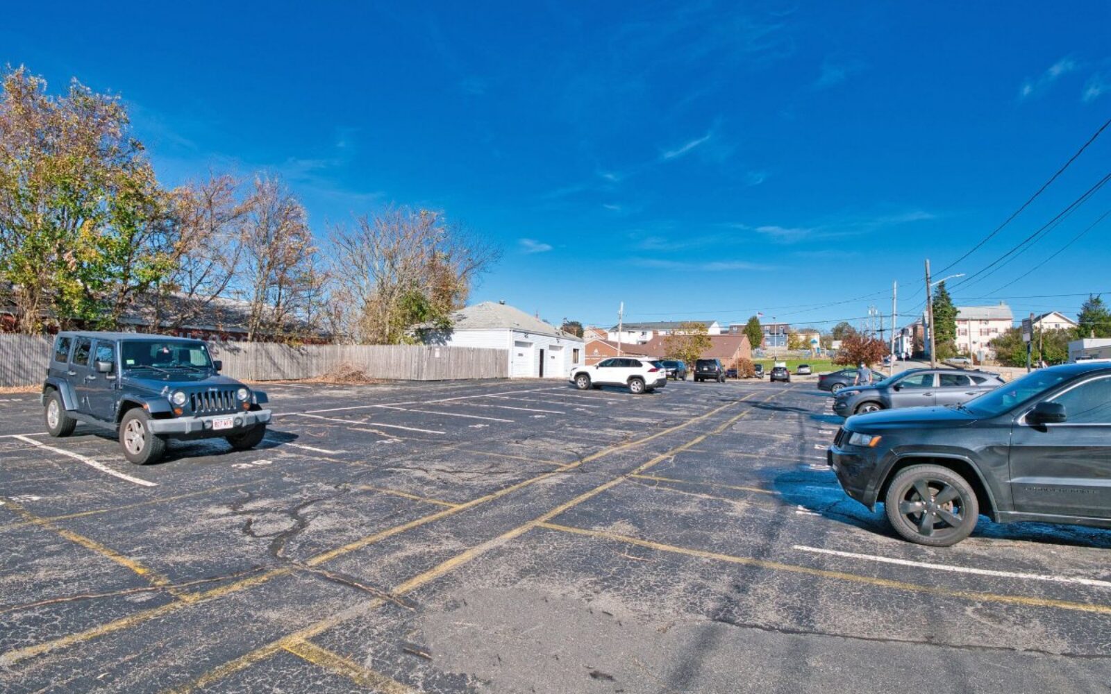 A mostly empty parking lot with several parked cars and a clear blue sky in the background.