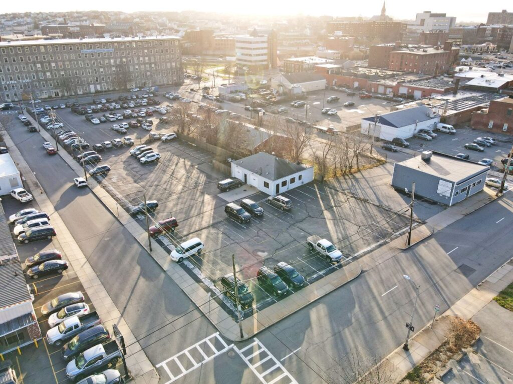 Aerial view of a parking lot with numerous cars, surrounded by buildings and casting long shadows.