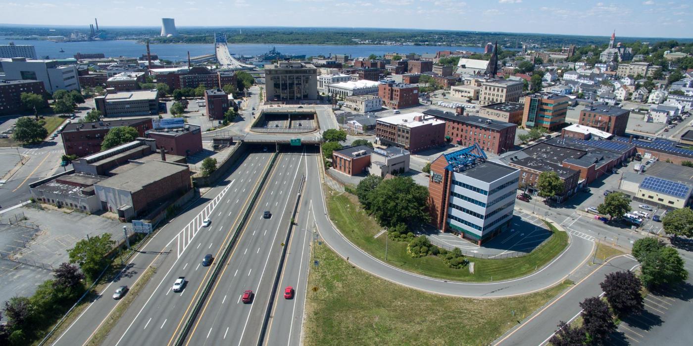 Aerial view of a city with a highway, buildings, and a river in the background.